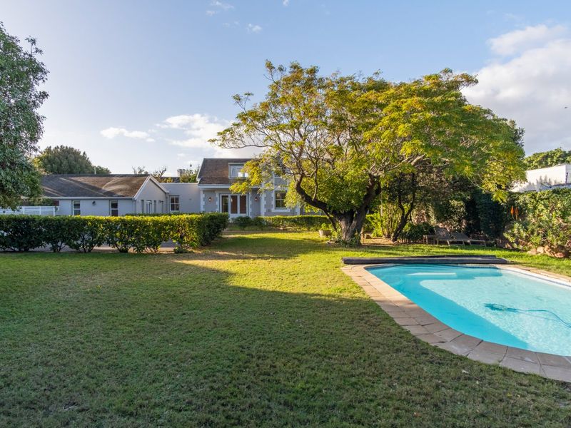 A spacious rear garden featuring a well-maintained swimming pool, mature trees, and established hedging, providing a private outdoor setting for the property.