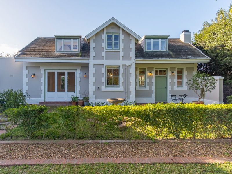 A charming rear elevation of a house featuring a pitched roof with dormer windows, a chimney, and a well-maintained garden with a brick-paved path.