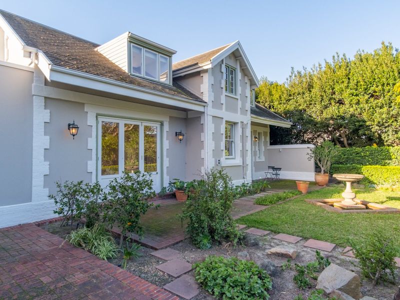 A well-maintained rear garden featuring a brick-paved patio, a stone fountain, and a charming house facade with dormer windows and french doors.
