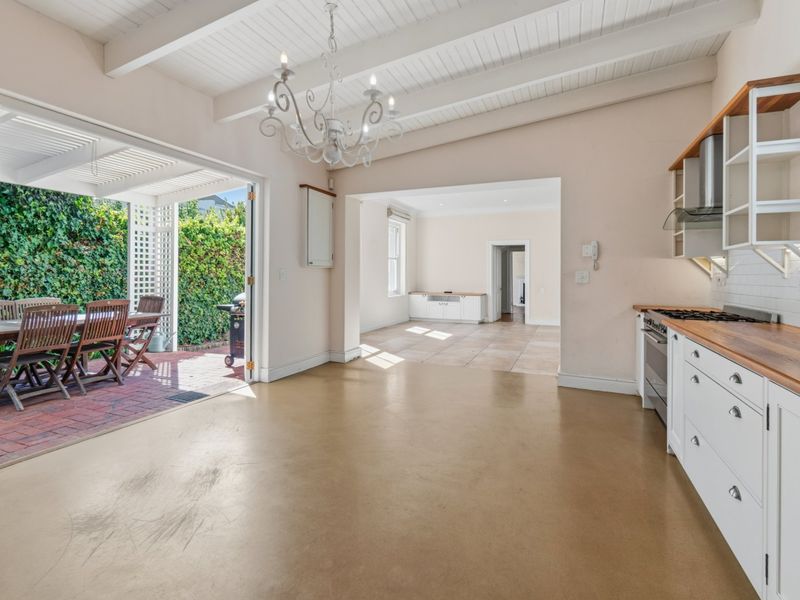 Spacious open-plan kitchen and living area featuring exposed beam ceilings, shaker-style cabinetry with timber countertops, and seamless flow to an outdoor patio.