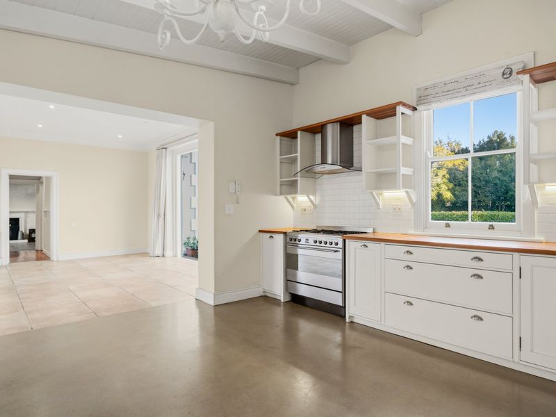 A bright, open-plan kitchen featuring shaker-style cabinetry, timber countertops, a stainless steel gas stove, and subway tile backsplash, with polished concrete flooring.