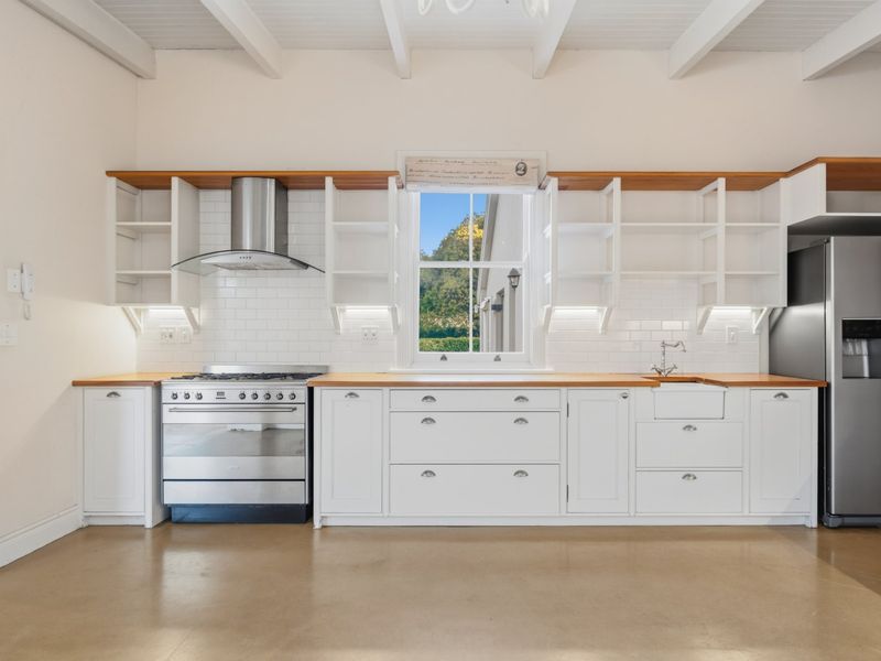 Modern farmhouse-style kitchen featuring white cabinetry, wooden countertops, subway tile backsplash, gas stove, and exposed ceiling beams with polished concrete flooring.