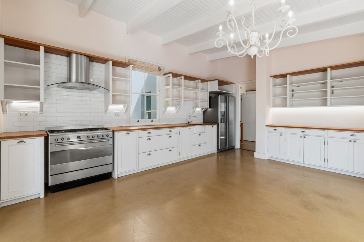 Spacious, light-filled kitchen featuring white cabinetry, wooden countertops, subway tile backsplash, stainless steel gas stove, and exposed white ceiling beams.