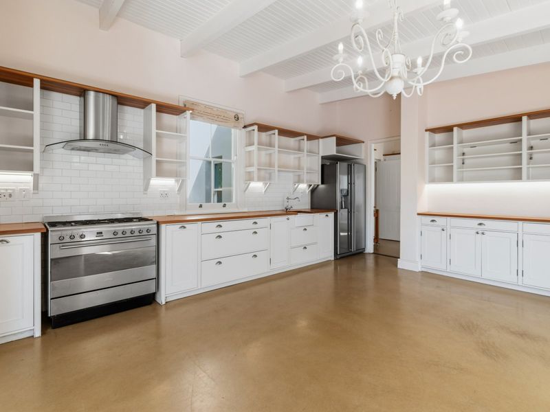 Spacious, light-filled kitchen featuring white cabinetry, wooden countertops, subway tile backsplash, stainless steel gas stove, and exposed white ceiling beams.