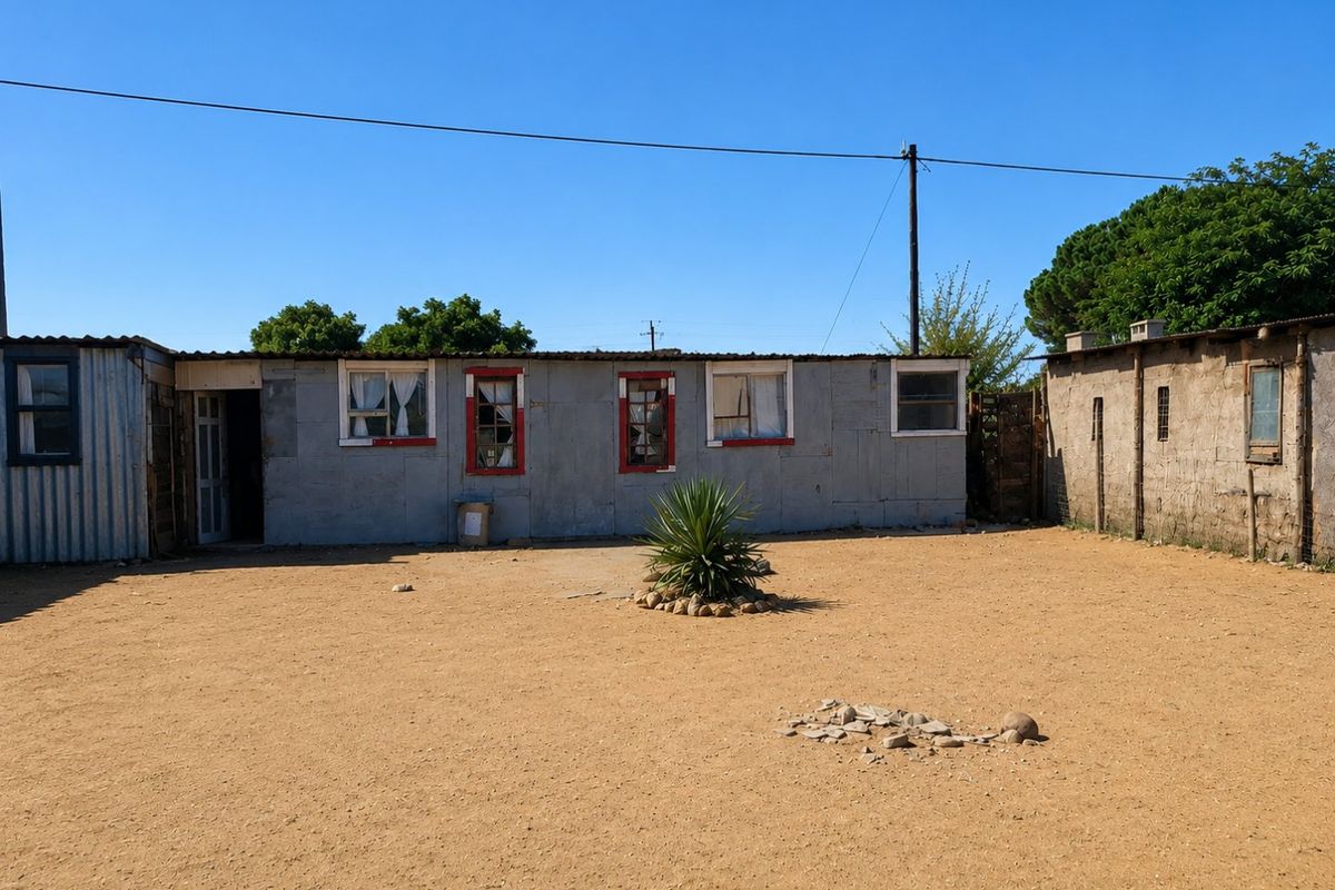 A view of a residential property exterior featuring corrugated metal and concrete block structures with a sandy yard area.