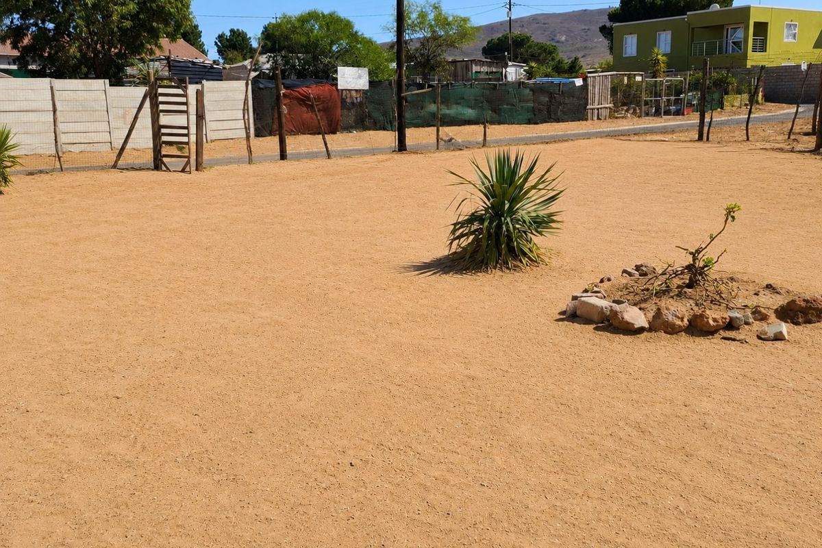 A vacant residential plot featuring sandy ground, perimeter fencing, and basic utility infrastructure.