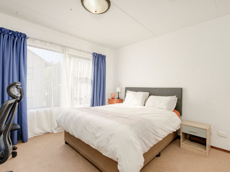 A well-lit bedroom featuring neutral carpet flooring, a large window with curtains, and a standard flush mount ceiling light fixture.