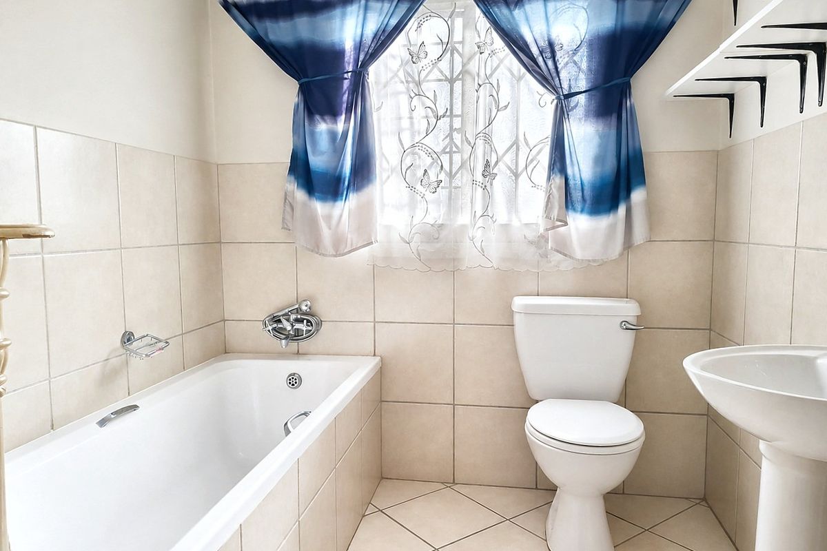 A functional bathroom featuring a built-in bathtub, pedestal basin, and ceramic toilet, finished with neutral wall and floor tiling.