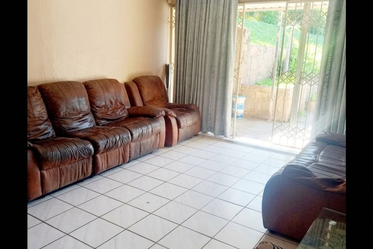 A living room featuring tiled flooring and a sliding glass door with security gate, providing direct access to the outdoor patio area.