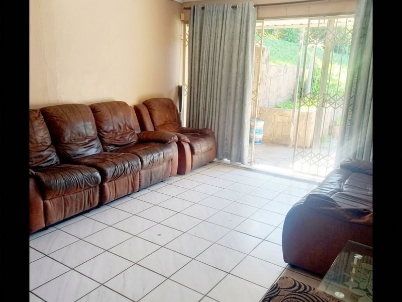 A living room featuring tiled flooring and a sliding glass door with security gate, providing direct access to the outdoor patio area.