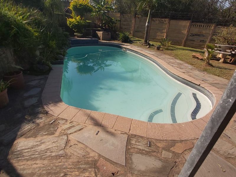 Outdoor swimming pool area featuring stone paving, integrated pool steps, and a surrounding precast concrete boundary wall in a landscaped garden setting.