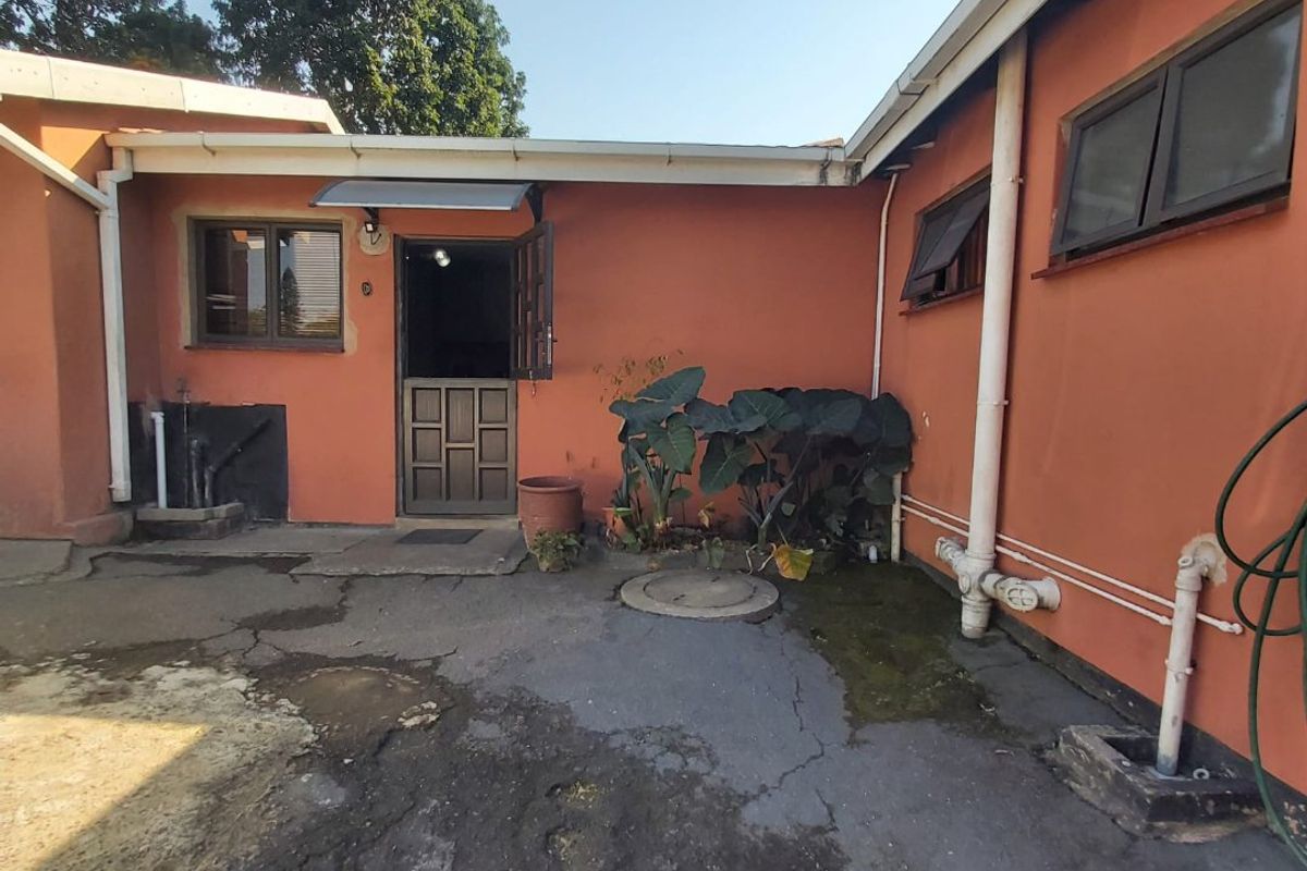 Rear exterior view of the property featuring a paved courtyard area, external access door, and weathered wall finishes requiring maintenance.