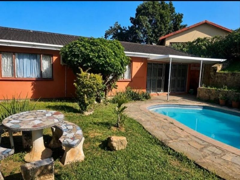 Rear garden area featuring a swimming pool with stone paving and a covered patio attached to the main house structure.