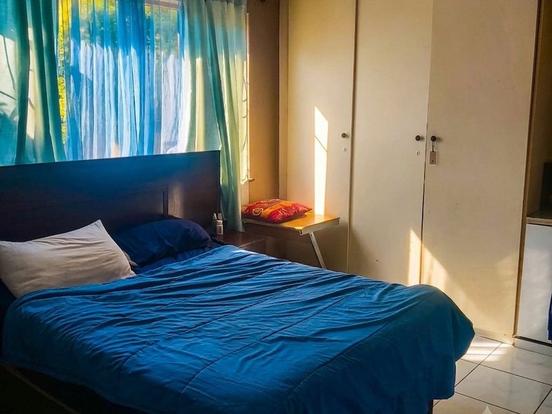 A bedroom featuring built-in cupboards and tiled flooring, benefiting from natural light through the window.