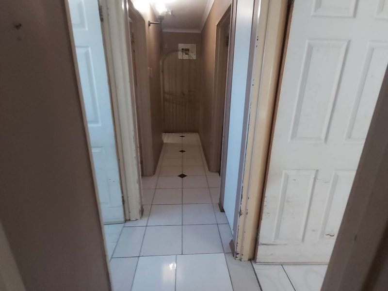 A functional hallway featuring white tiled flooring and multiple interior panel doors, providing access to various rooms within the home.