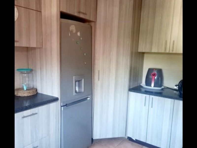 A functional kitchen featuring light wood-grain laminate cabinetry, dark countertops, and tiled flooring, providing ample storage and workspace.