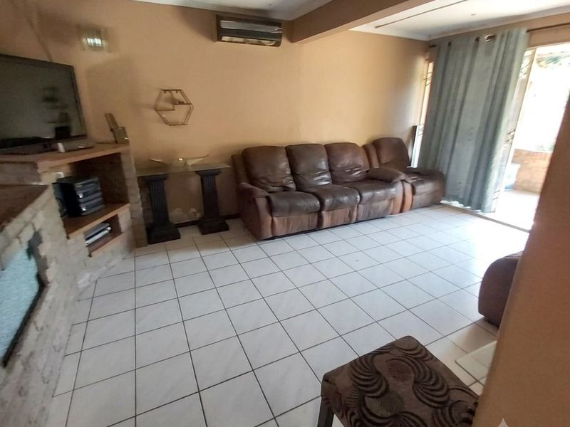 A living room featuring tiled flooring, a built-in brick fireplace, and a split-system air conditioner, with direct access to an outdoor patio area.