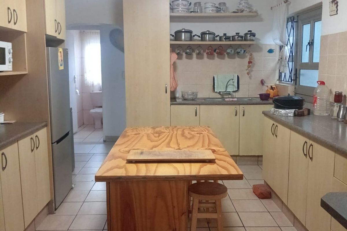 A functional kitchen featuring laminate cabinetry, tiled flooring, and a central wooden island, offering a practical layout with potential for modern updates.
