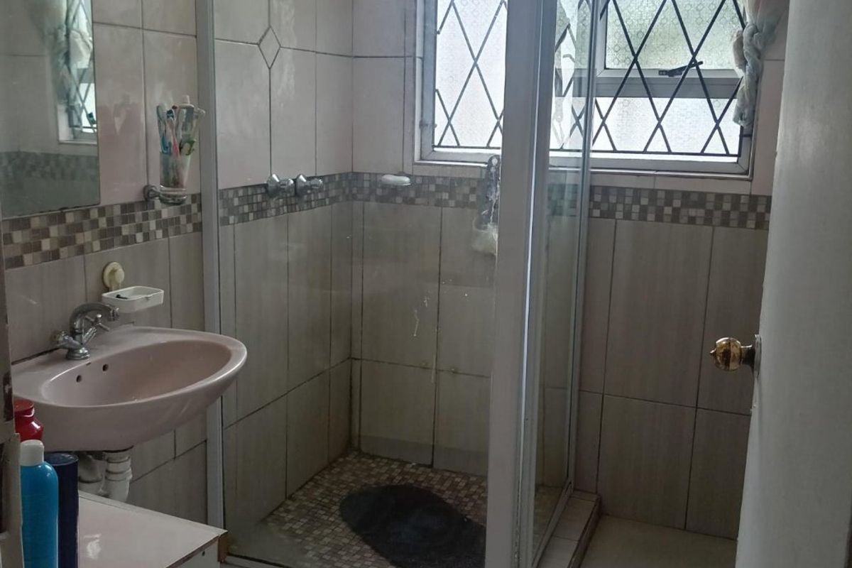 A functional bathroom featuring a shower enclosure, pedestal basin, and tiled finishes, offering potential for modernization and cosmetic updates.