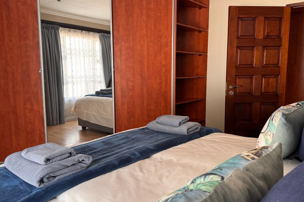 A bedroom featuring built-in wooden wardrobes with mirrored panels, a solid wood door, and laminate flooring.