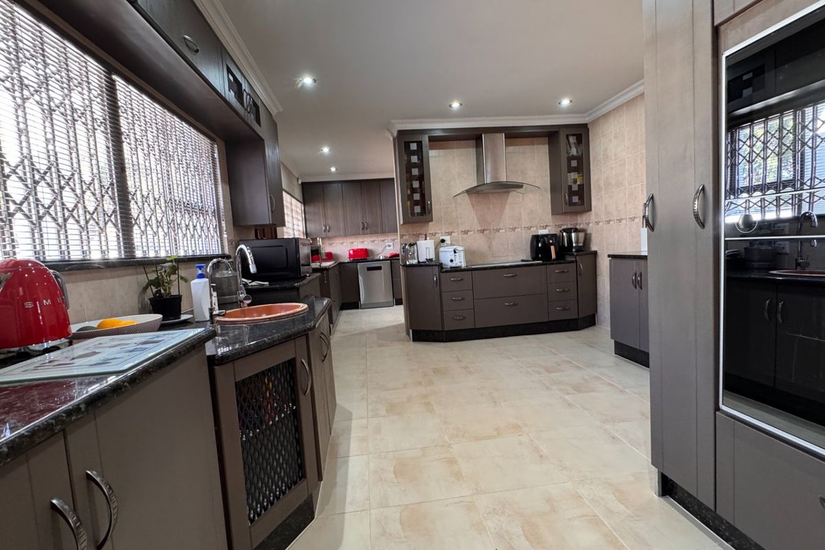 Spacious kitchen featuring dark cabinetry, granite countertops, integrated oven, extractor fan, and tiled flooring with ample natural light.