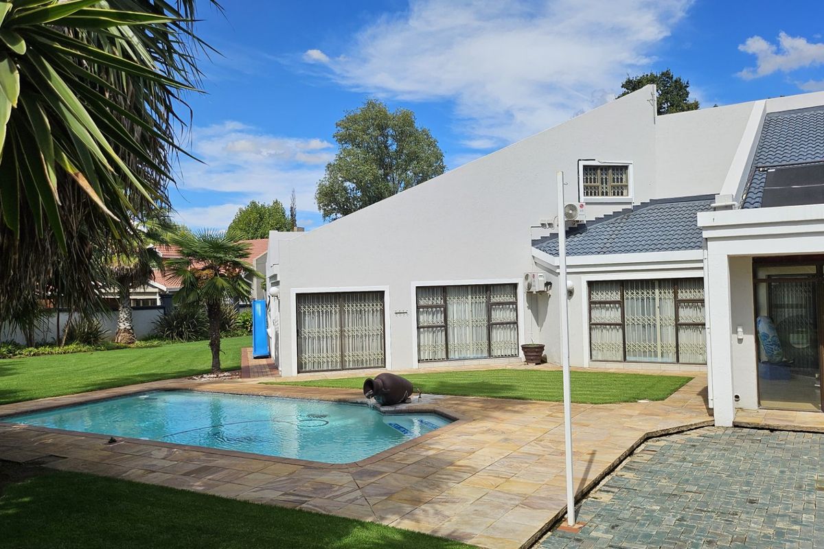 Rear view of the property featuring a well-maintained swimming pool, stone paved patio area, and a spacious lawn.