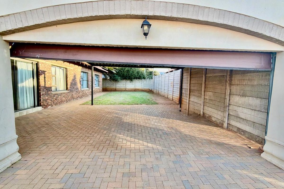 Rear exterior view of the townhouse featuring a paved driveway, covered patio area, and a private garden enclosed by precast concrete boundary walls.