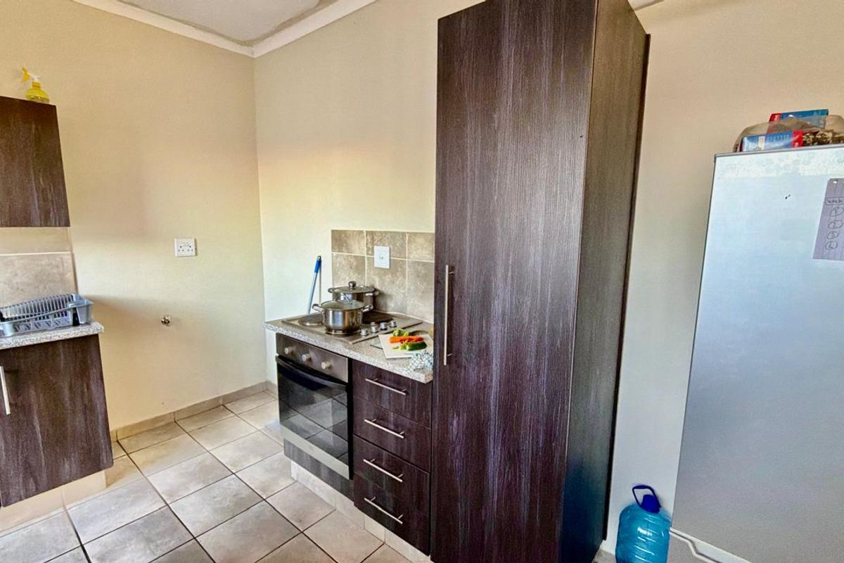 Compact kitchen featuring dark wood-look cabinetry, tiled splashbacks, built-in oven and hob, and tiled flooring.
