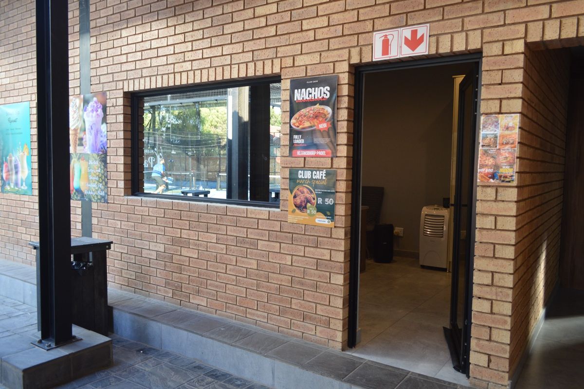 Exterior view of a commercial brick building featuring a service window and entrance, with tiled flooring and clear signage.
