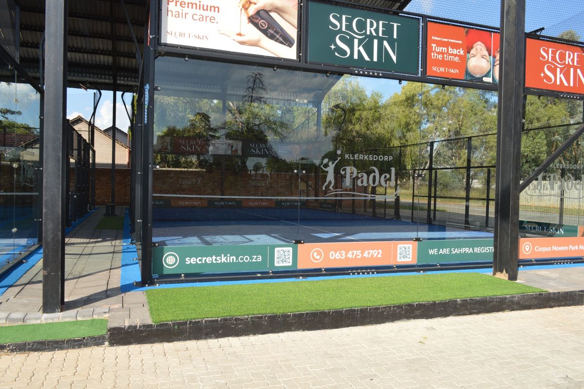 A well-maintained outdoor padel court featuring a steel frame, tempered glass walls, and synthetic turf surface, currently utilized for commercial branding.
