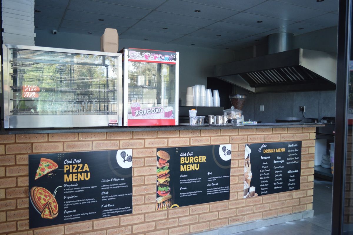 A commercial cafe service counter featuring a brick facade, granite countertop, and professional-grade extractor hood for food preparation.