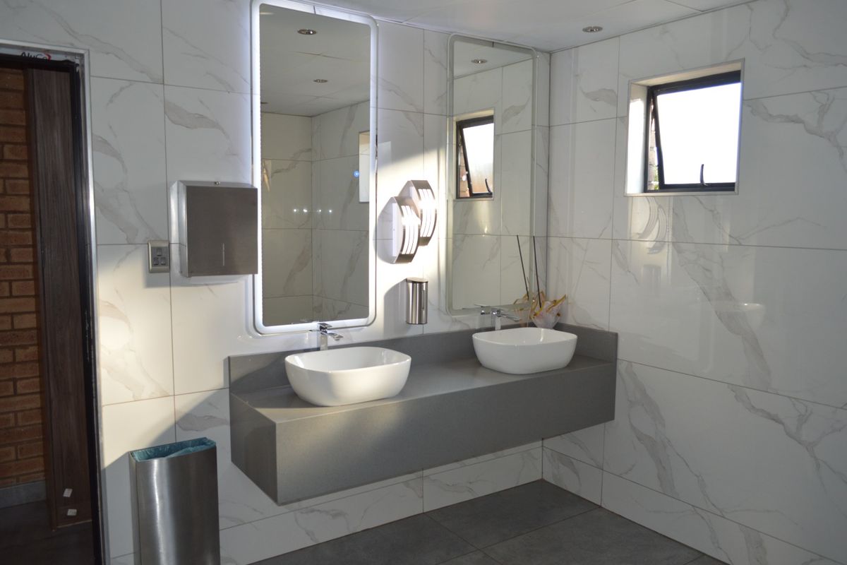 Modern commercial bathroom featuring a floating double vanity with vessel sinks, marble-look wall tiling, and integrated LED-lit mirrors.