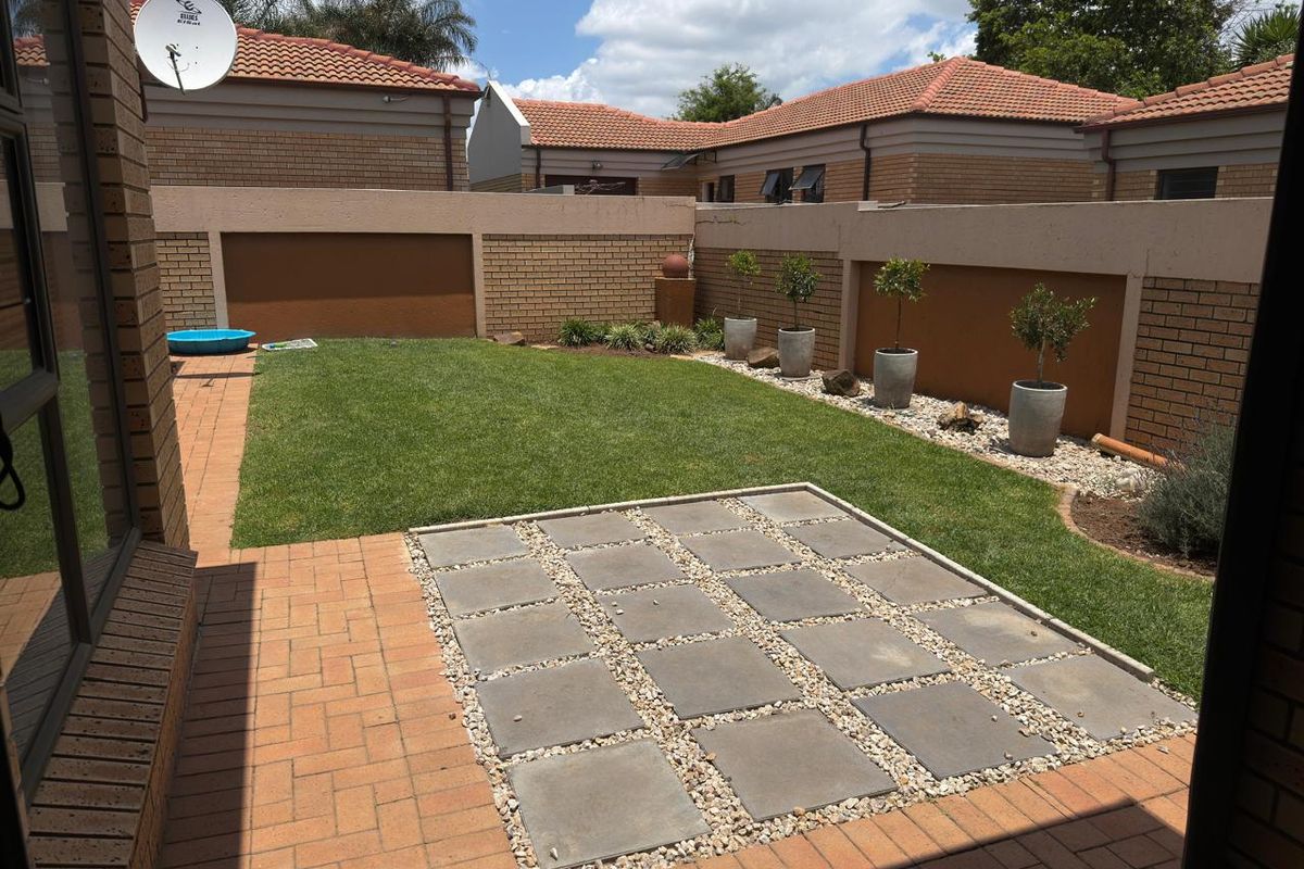 A well-maintained rear garden featuring a paved patio area, manicured lawn, and enclosed brick boundary walls.