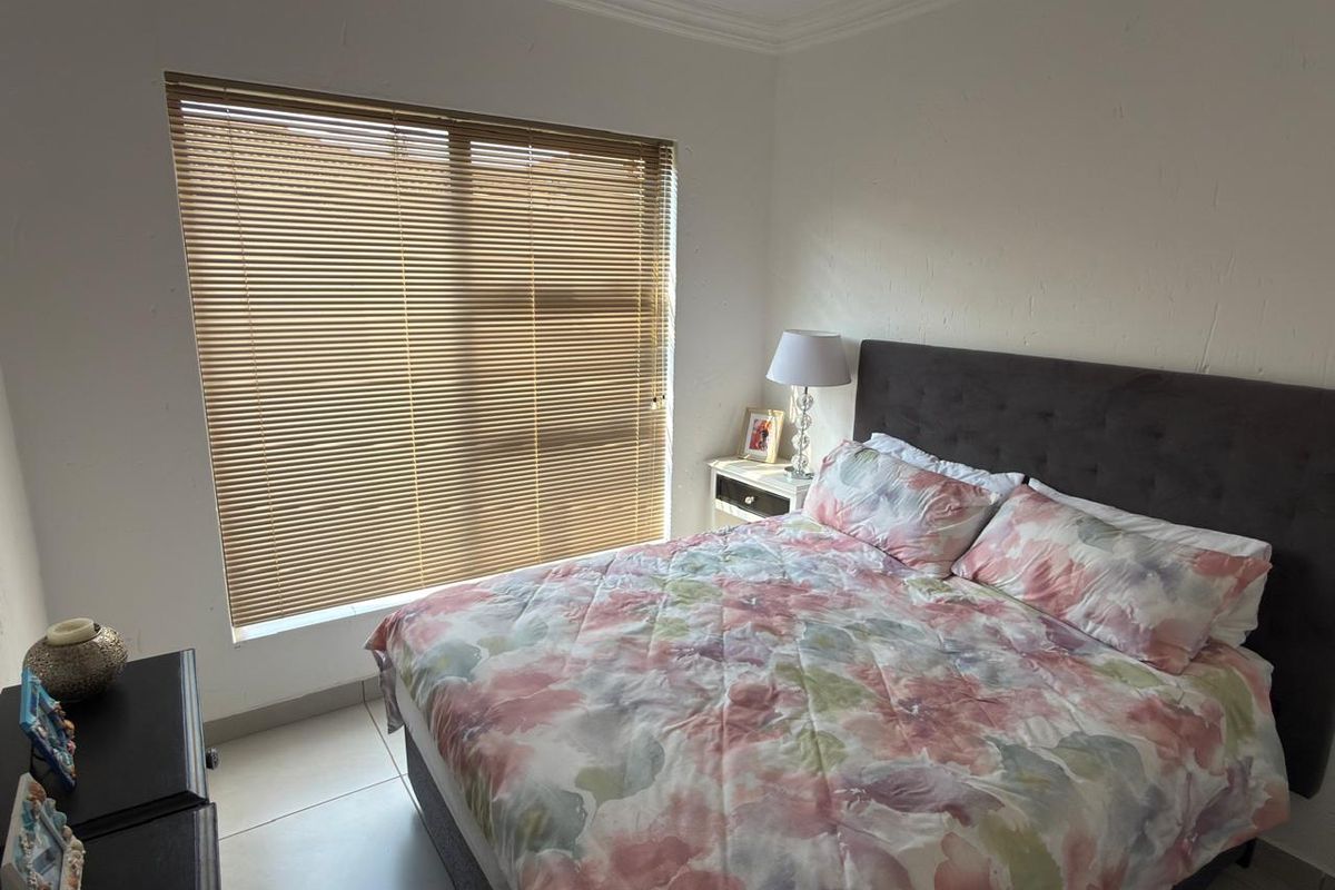 A functional bedroom featuring tiled flooring, neutral wall finishes, and venetian blinds, providing a comfortable and well-lit sleeping space.