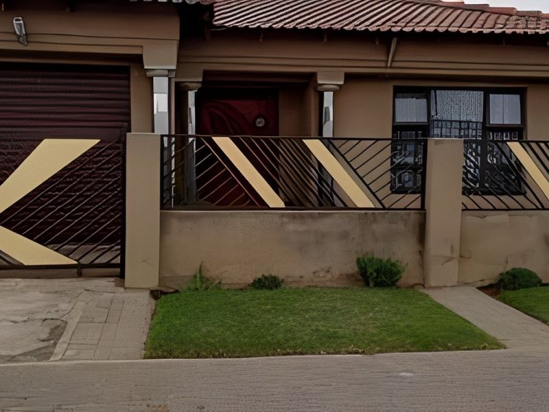 Front elevation of the house featuring a roller garage door, secure boundary wall with metal fencing, and a paved driveway entrance.