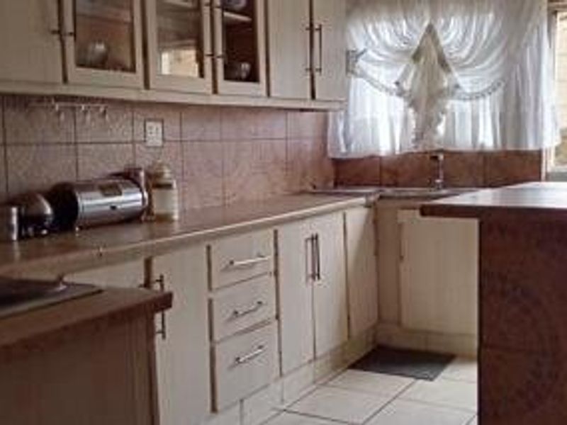 A dated kitchen featuring laminate cabinetry, tiled backsplash, and tiled flooring, offering a functional layout with potential for modern renovation.