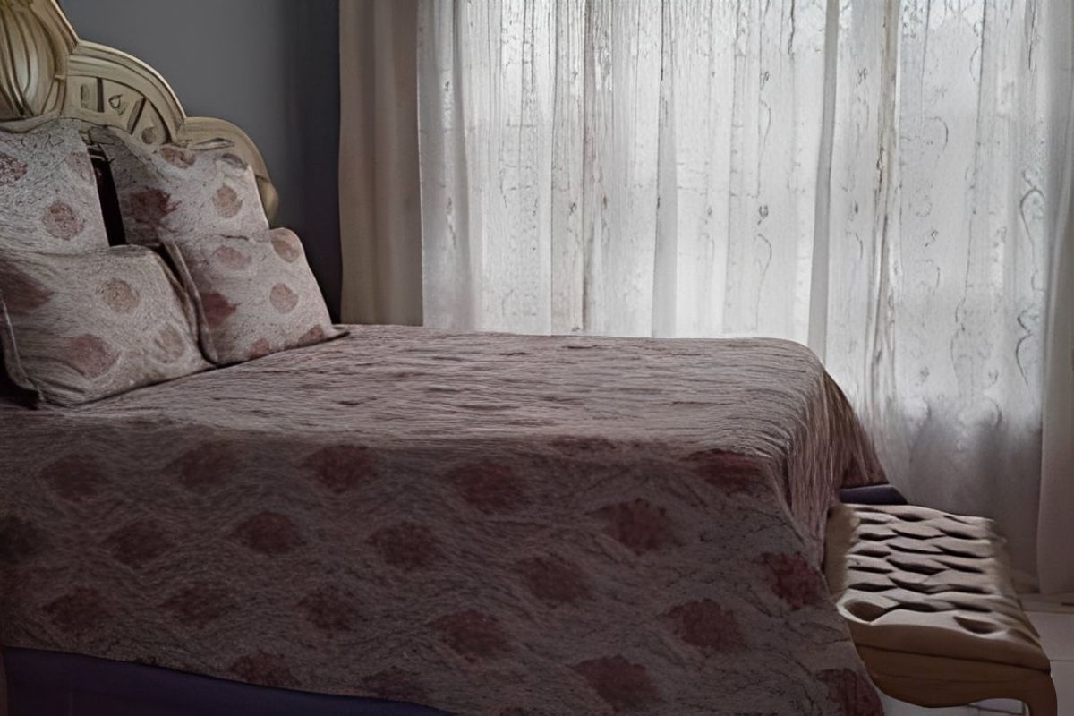 A bedroom interior featuring a bed positioned against a window with sheer curtains.