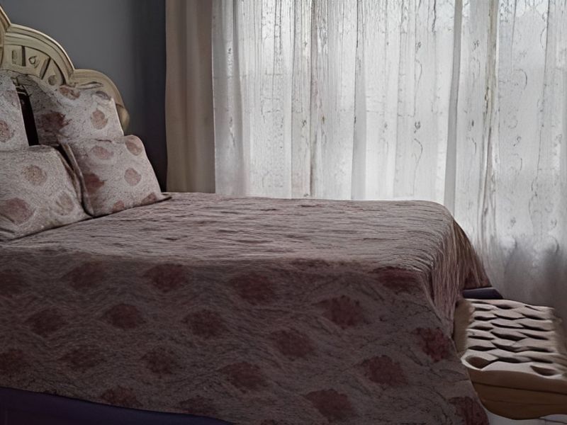 A bedroom interior featuring a bed positioned against a window with sheer curtains.