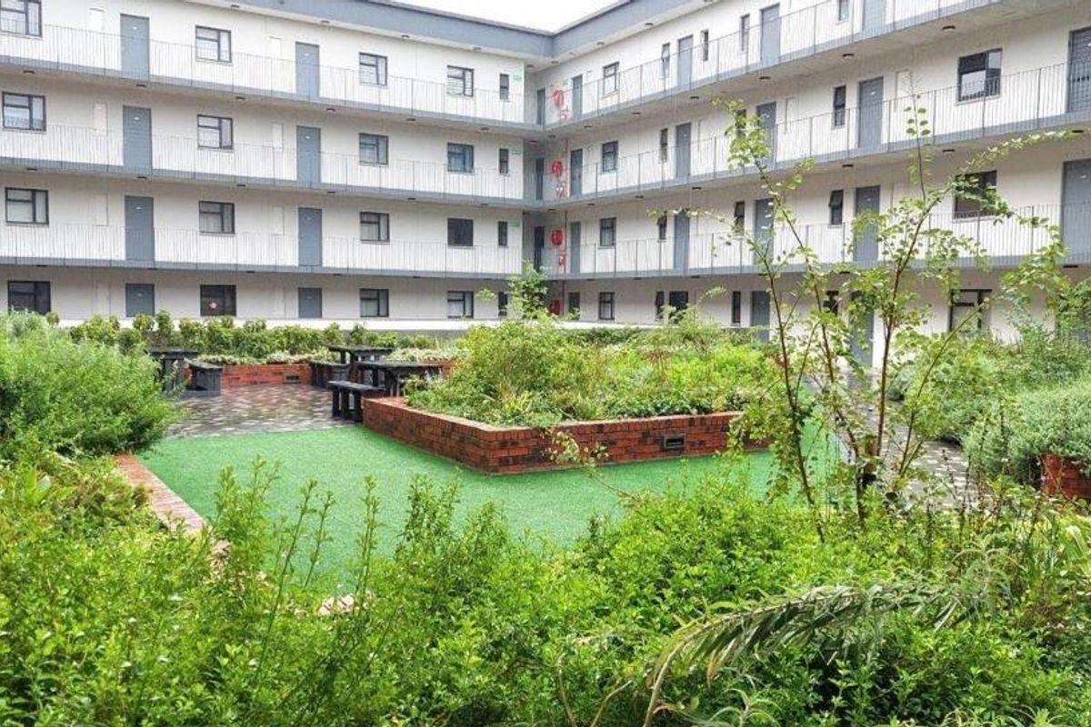 A landscaped courtyard area within an apartment complex, featuring brick planter boxes, artificial turf, and paved walkways surrounded by multi-story residential units.