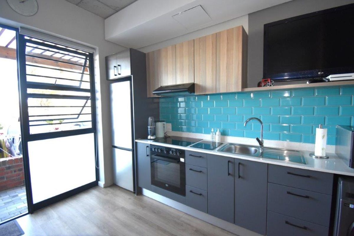 Modern kitchen featuring sleek grey and wood-tone cabinetry, a vibrant blue subway tile backsplash, integrated appliances, and durable laminate flooring.