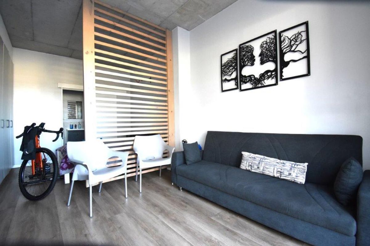Modern living area featuring an exposed concrete ceiling, timber slat room divider, and durable laminate flooring in an open-plan apartment layout.