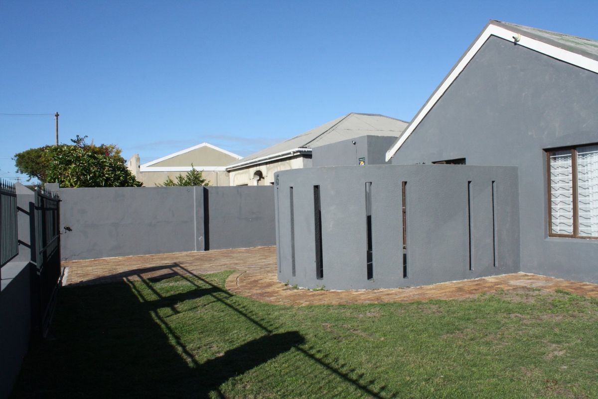 A private rear courtyard featuring a paved patio area, a curved feature wall, and a small lawn enclosed by boundary walls.
