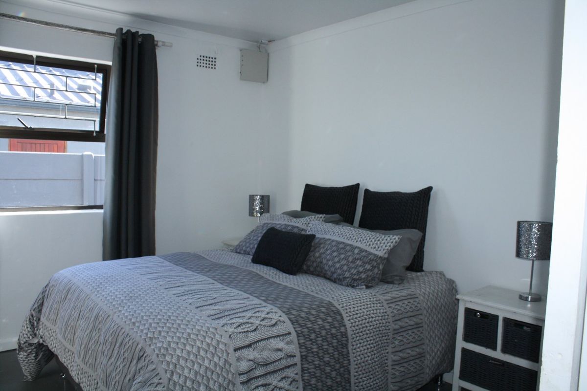 A bedroom featuring a window with security bars and a wall-mounted ventilation brick.