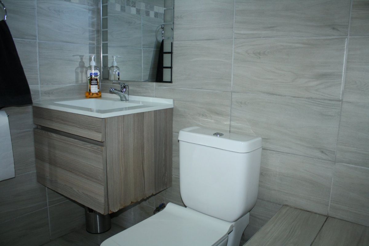 A modern bathroom featuring a wall-mounted vanity with a ceramic basin, chrome tapware, and neutral wood-look wall tiles.