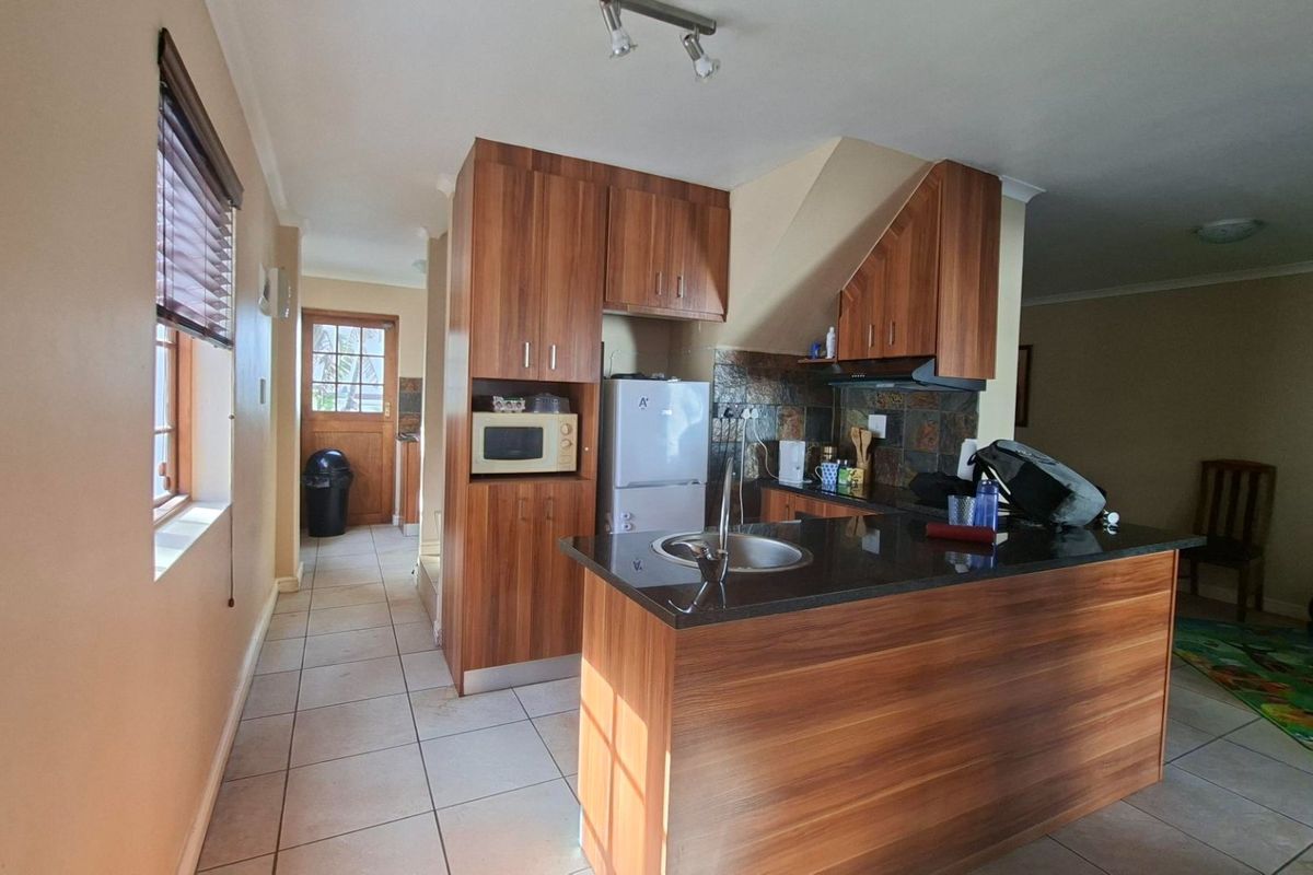 A functional kitchen featuring wood-veneer cabinetry, granite countertops, a stainless steel sink, and a slate tile backsplash with tiled flooring throughout.