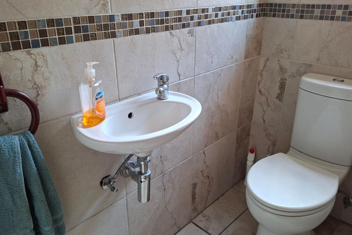 A compact bathroom featuring a wall-mounted basin with chrome fixtures, a close-coupled toilet, and neutral ceramic wall tiling with a decorative mosaic border.