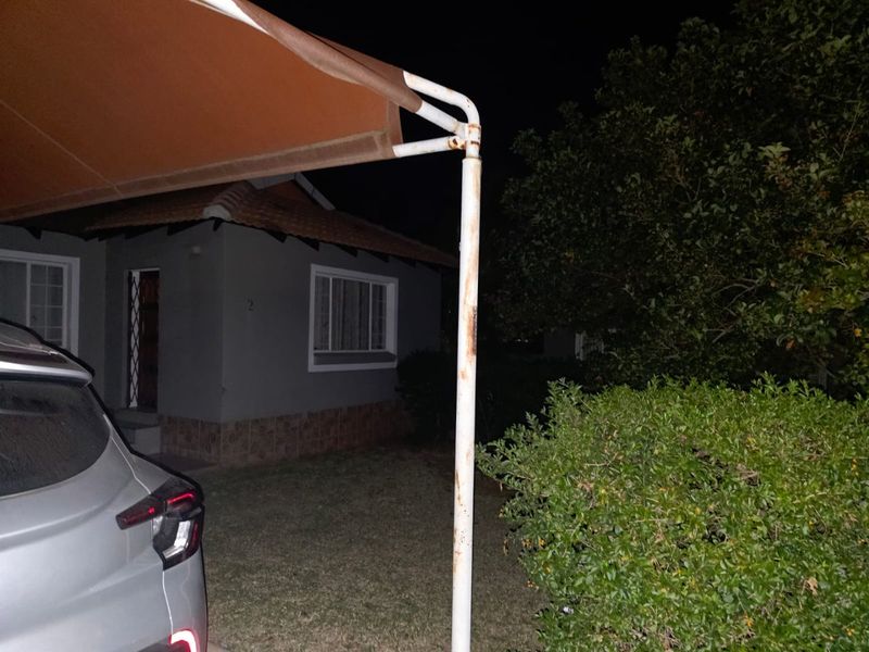 Night view of the front exterior of the townhouse, featuring a carport with a rusted support structure and a small front garden area.