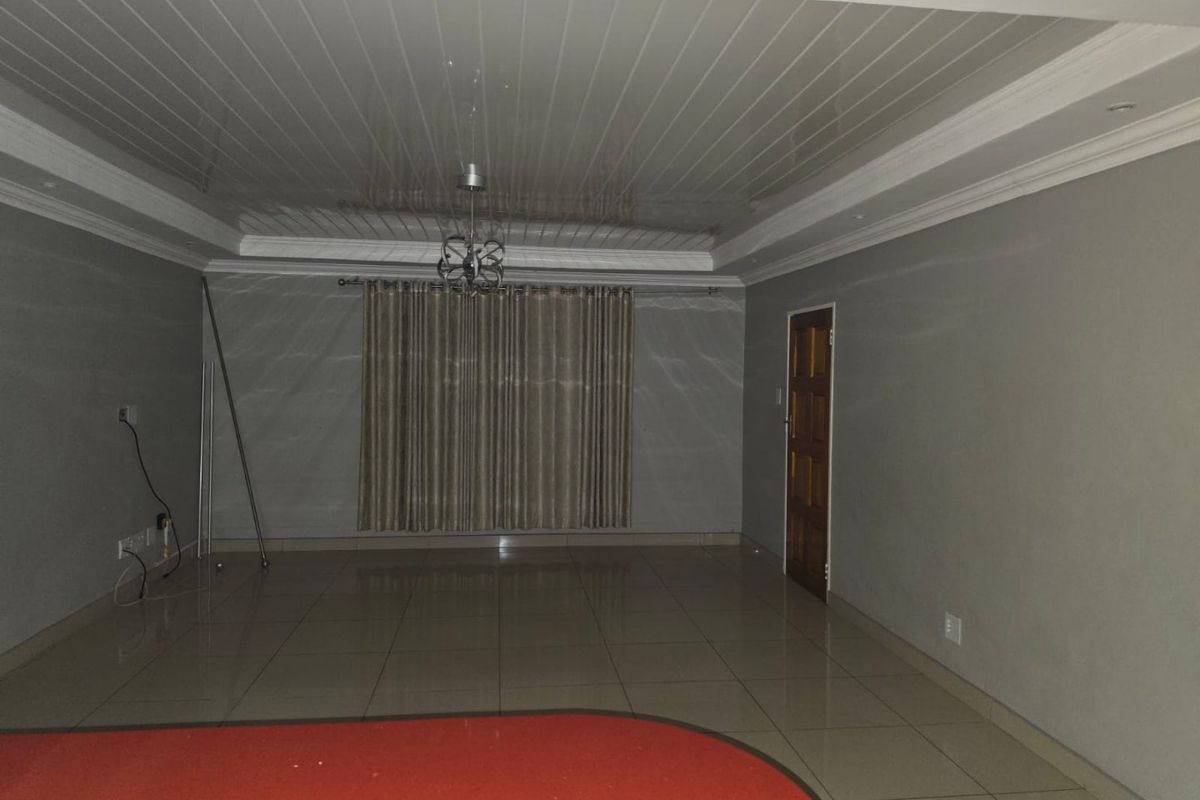 Spacious, empty living area featuring glossy ceiling finishes, tiled flooring, and a wooden door, providing a blank canvas for interior design.