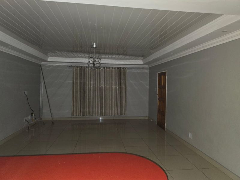 Spacious, empty living area featuring glossy ceiling finishes, tiled flooring, and a wooden door, providing a blank canvas for interior design.