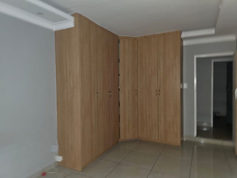 A bedroom featuring light wood-finish built-in cupboards, neutral tiled flooring, and coved ceiling detailing.